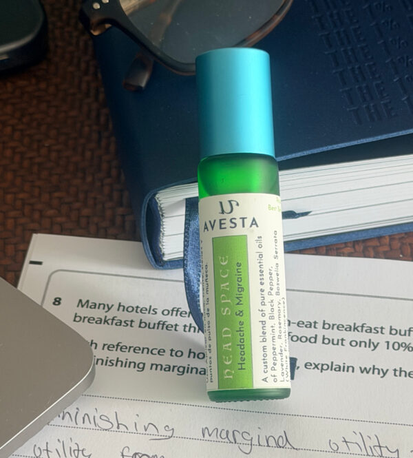 Avesta Head Space essential oil roll-on bottle in green glass with a turquoise cap, placed on a notebook and study papers on a desk.