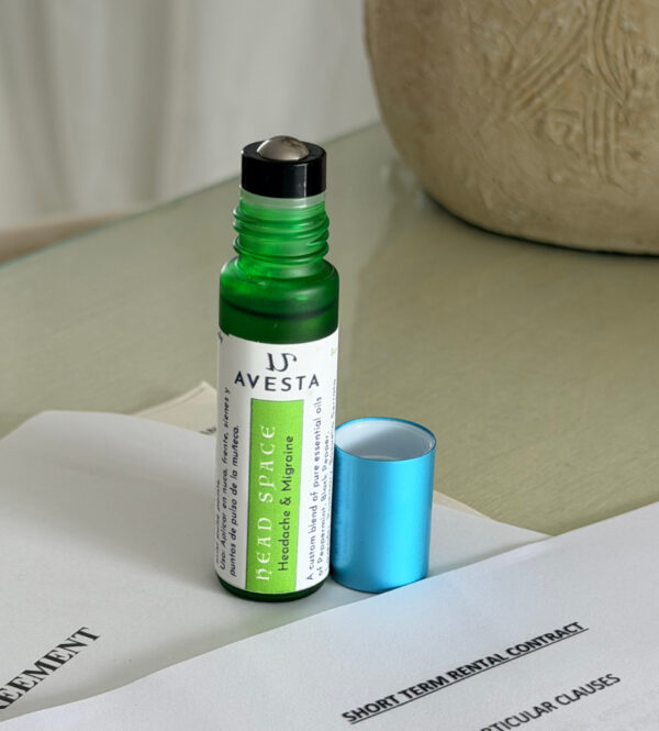 Avesta Head Space essential oil roll-on bottle in green glass bottle with a turquoise cap next to it, placed on a contract agreement on a table.