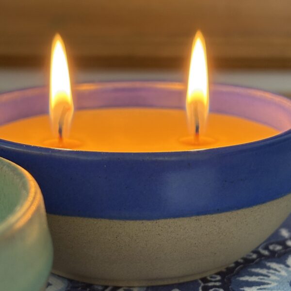 Beeswax Candle in Handmade Pottery Lit beeswax candle in handmade blue rimmed pottery bowl