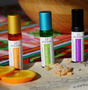 Avesta Morning Mate essential oil blend in an amber glass roller bottle with a gold cap, styled with fresh orange slices on a colourful textile background.